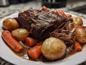 A close-up of a tender slow cooker pot roast, surrounded by carrots and potatoes, in a rich gravy.