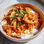 A bowl of creamy slow cooker sweet chili chicken served over white rice and topped with chopped green onions.