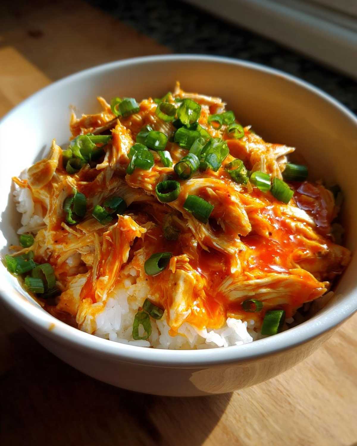 A bowl of white rice topped with shredded slow cooker sweet chili chicken and chopped green onions.