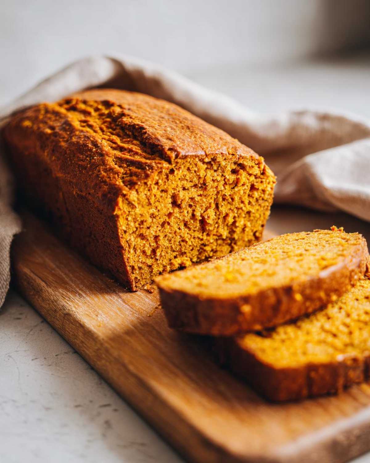 A loaf of moist sourdough pumpkin bread, partially sliced, on a wooden cutting board.