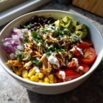 A vibrant Southwest chicken salad bowl overflowing with shredded chicken, black beans, corn, avocado, tomatoes, and red onion, drizzled with dressing.