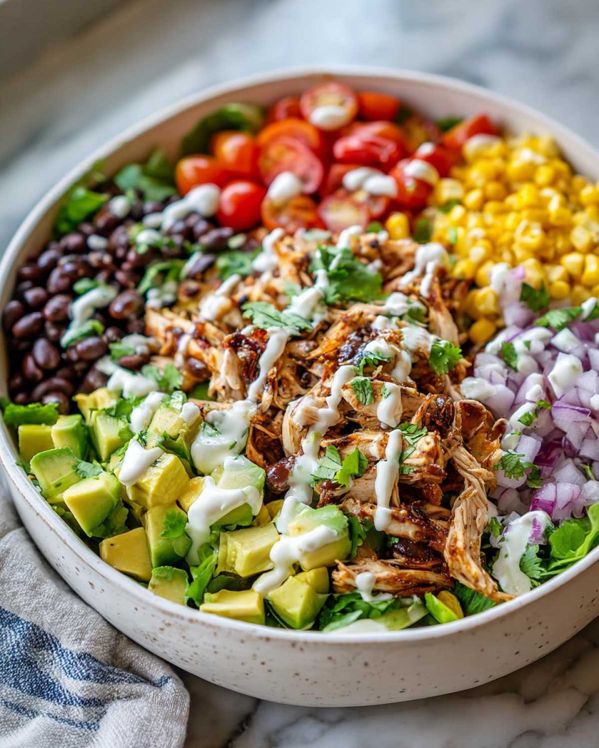 A vibrant bowl of Southwest chicken salad featuring shredded chicken, black beans, corn, tomatoes, avocado, and red onion, drizzled with a creamy dressing.
