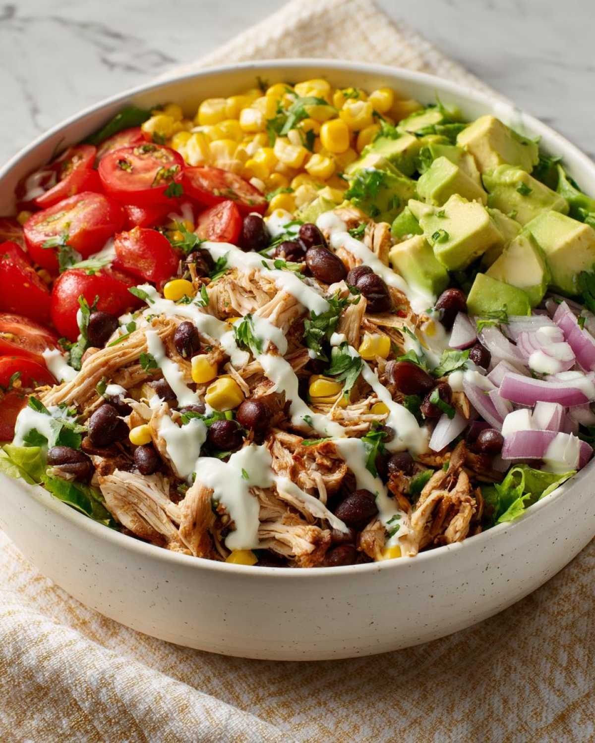 A vibrant Southwest chicken salad in a bowl, featuring shredded chicken, black beans, corn, tomatoes, avocado, and red onion, drizzled with dressing.