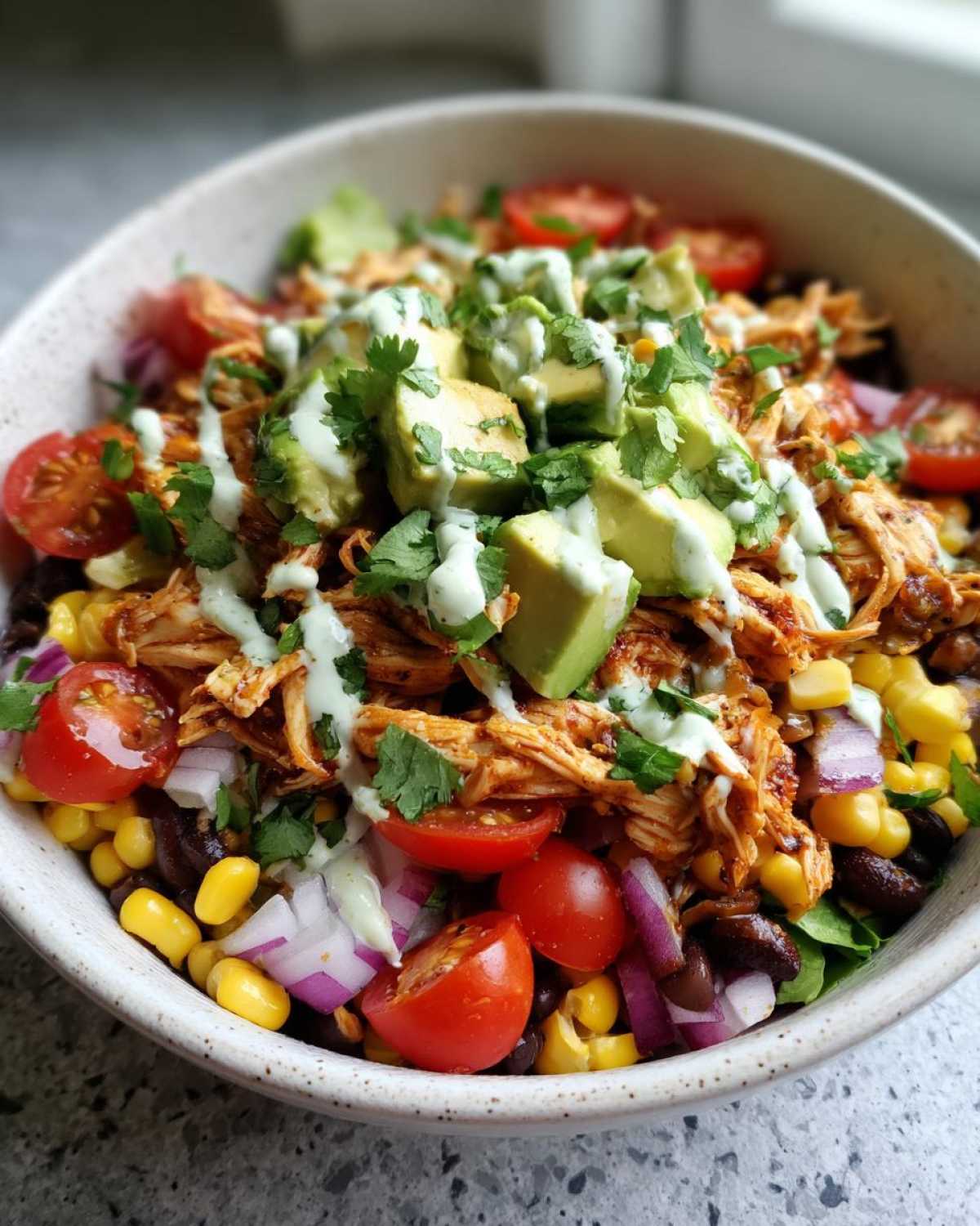 A vibrant Southwest chicken salad bowl filled with shredded chicken, black beans, corn, tomatoes, red onion, and avocado, drizzled with a creamy dressing.