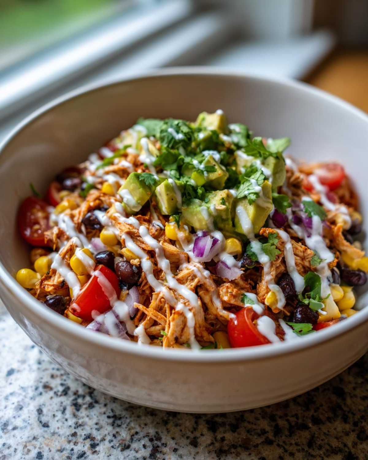 A close-up of a Southwest chicken salad bowl filled with shredded chicken, black beans, corn, tomatoes, red onion, avocado, and a creamy dressing.