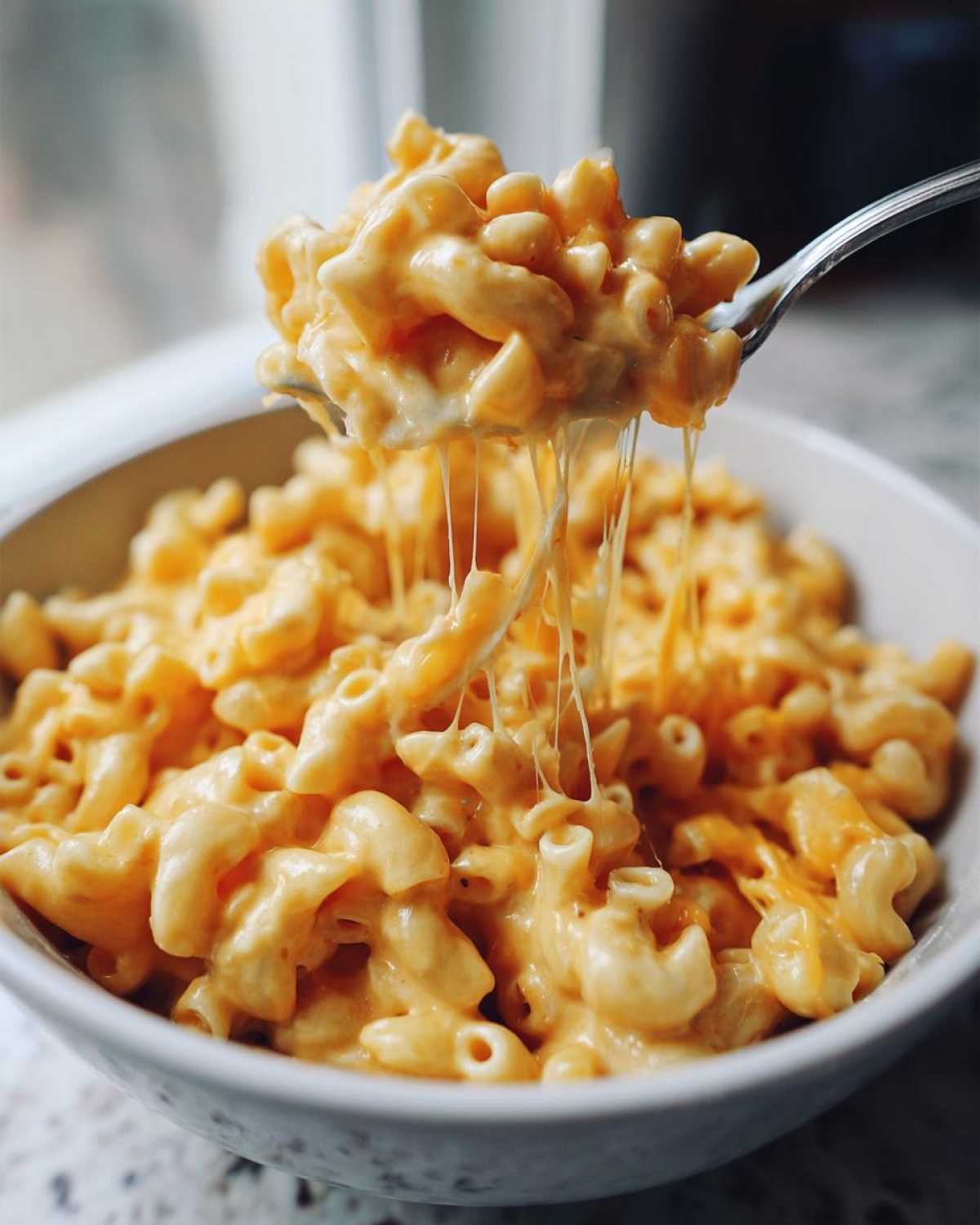 Close-up of a fork lifting creamy stovetop mac and cheese, showcasing a delicious cheese pull.