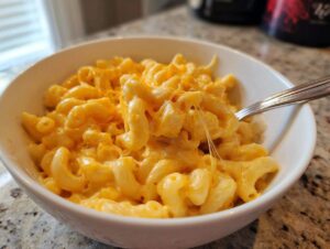 Close-up of creamy stovetop mac and cheese in a white bowl, with a fork lifting cheesy pasta.