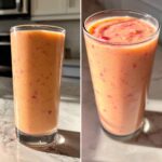 A tall glass filled with a vibrant strawberry mango smoothie, showing flecks of fruit throughout.