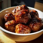 A white bowl filled with glistening sweet chili meatballs crockpot, garnished with herbs and spices, with steam rising.