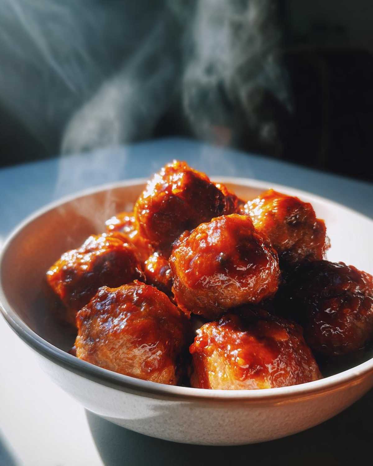 A bowl of steaming sweet chili meatballs crockpot, coated in a glossy sauce.