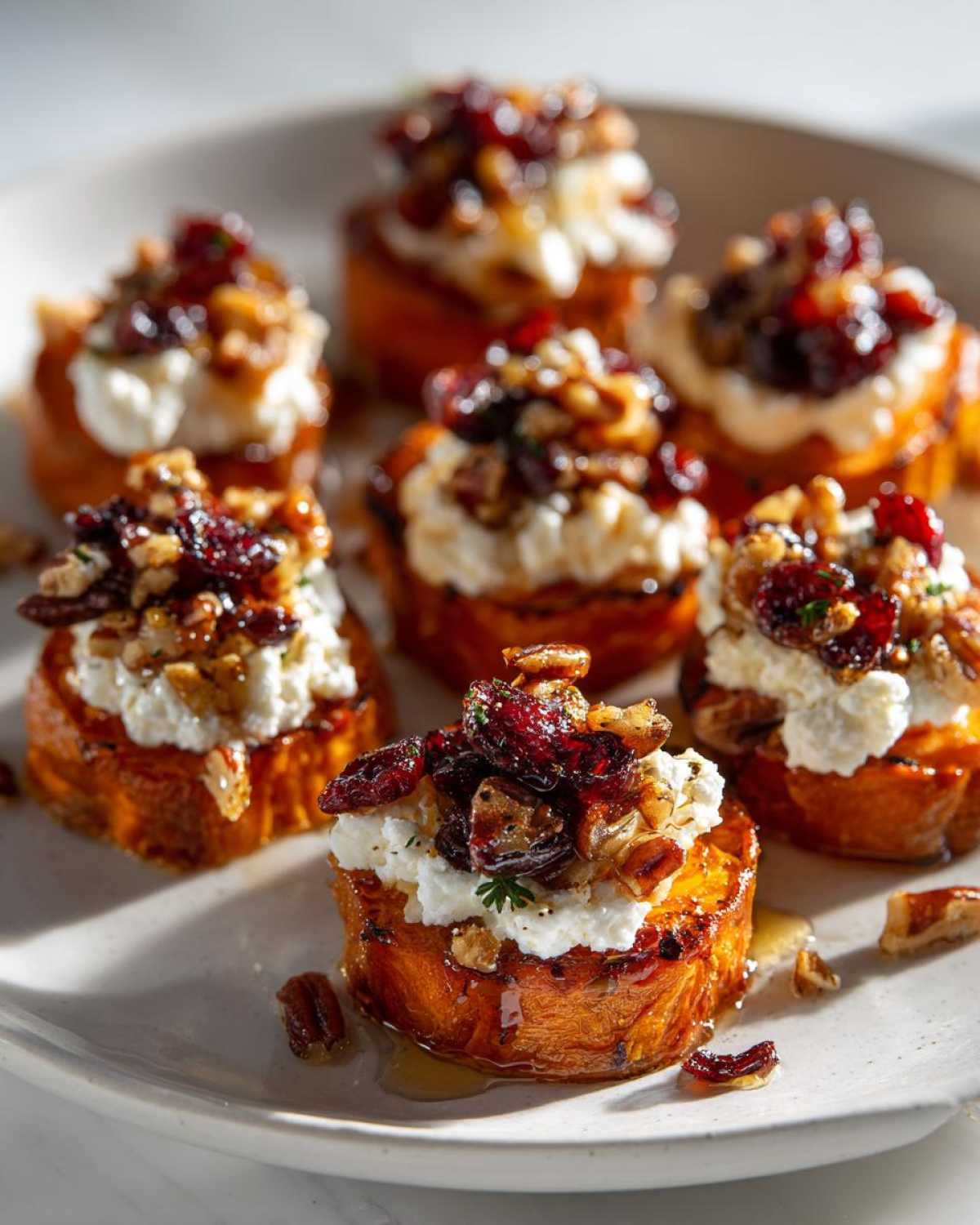 Close-up of sweet potato rounds topped with creamy goat cheese, dried cranberries, and toasted walnuts.