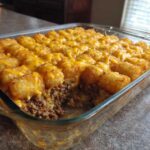 A close-up of a freshly baked tater tot casserole with ground beef and melted cheese in a glass baking dish.