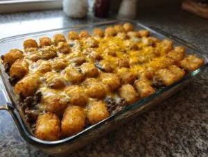 Golden brown tater tot casserole with ground beef and melted cheese in a glass baking dish.