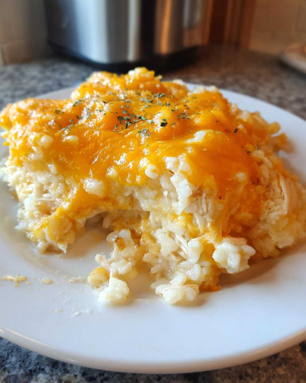 A scoop of creamy chicken rice casserole topped with melted cheddar cheese and sprinkled with dried parsley.