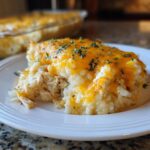 A close-up serving of creamy chicken and rice casserole topped with melted cheddar cheese and parsley.
