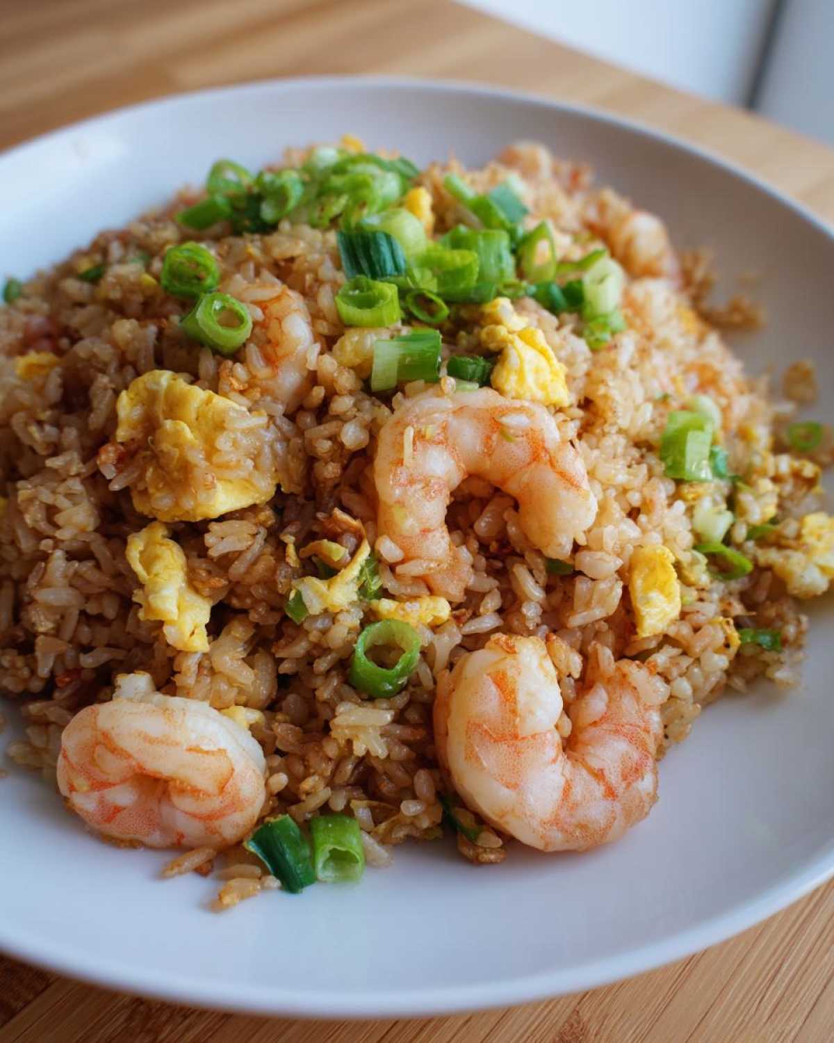 A close-up of a serving of savory shrimp fried rice, featuring plump shrimp, scrambled egg pieces, and fresh green onions.