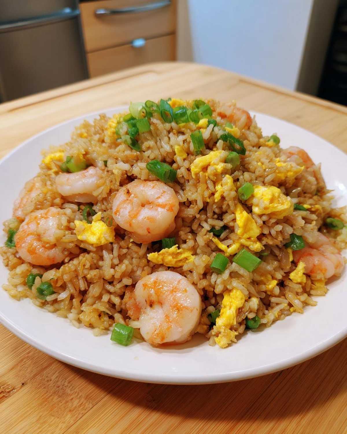 A close-up of a white plate piled high with delicious shrimp fried rice, featuring plump shrimp, scrambled egg, and green onions.