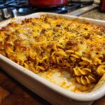 A close-up of a freshly baked Amish country casserole, featuring spiral pasta, seasoned ground meat, and melted cheese topping.