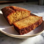 A close-up of a slice of moist apple cider pound cake, with a golden crust and tender crumb.