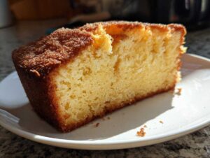 A slice of moist apple cider pound cake on a white plate, showcasing its golden-brown crust and tender crumb.