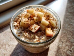 Close-up of apple cinnamon overnight oats in a glass jar topped with diced fresh apples and sprinkled cinnamon.