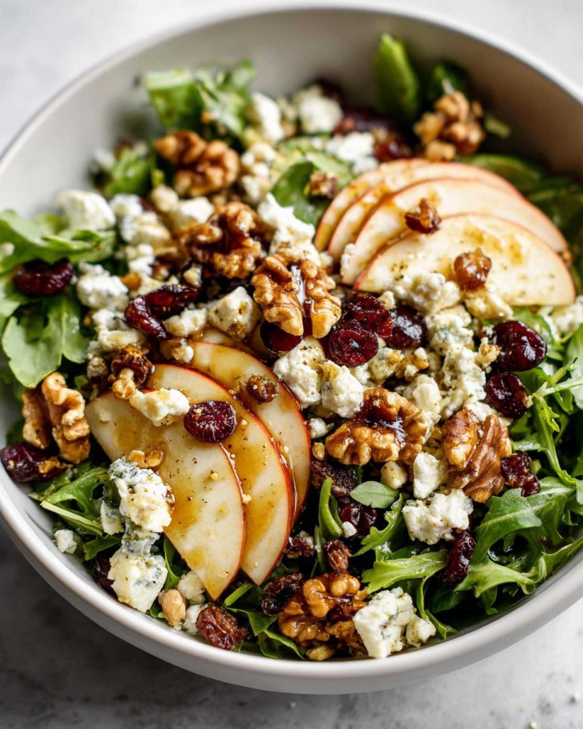 A close-up of a vibrant apple feta salad with arugula, sliced apples, crumbled feta cheese, walnuts, and dried cranberries.