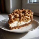 A decadent slice of apple pie cheesecake featuring a graham cracker crust, creamy filling, spiced apples, and a crumble topping.