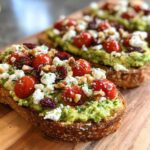 Close-up of avocado toast with feta cheese, cherry tomatoes, walnuts, and dried cranberries.