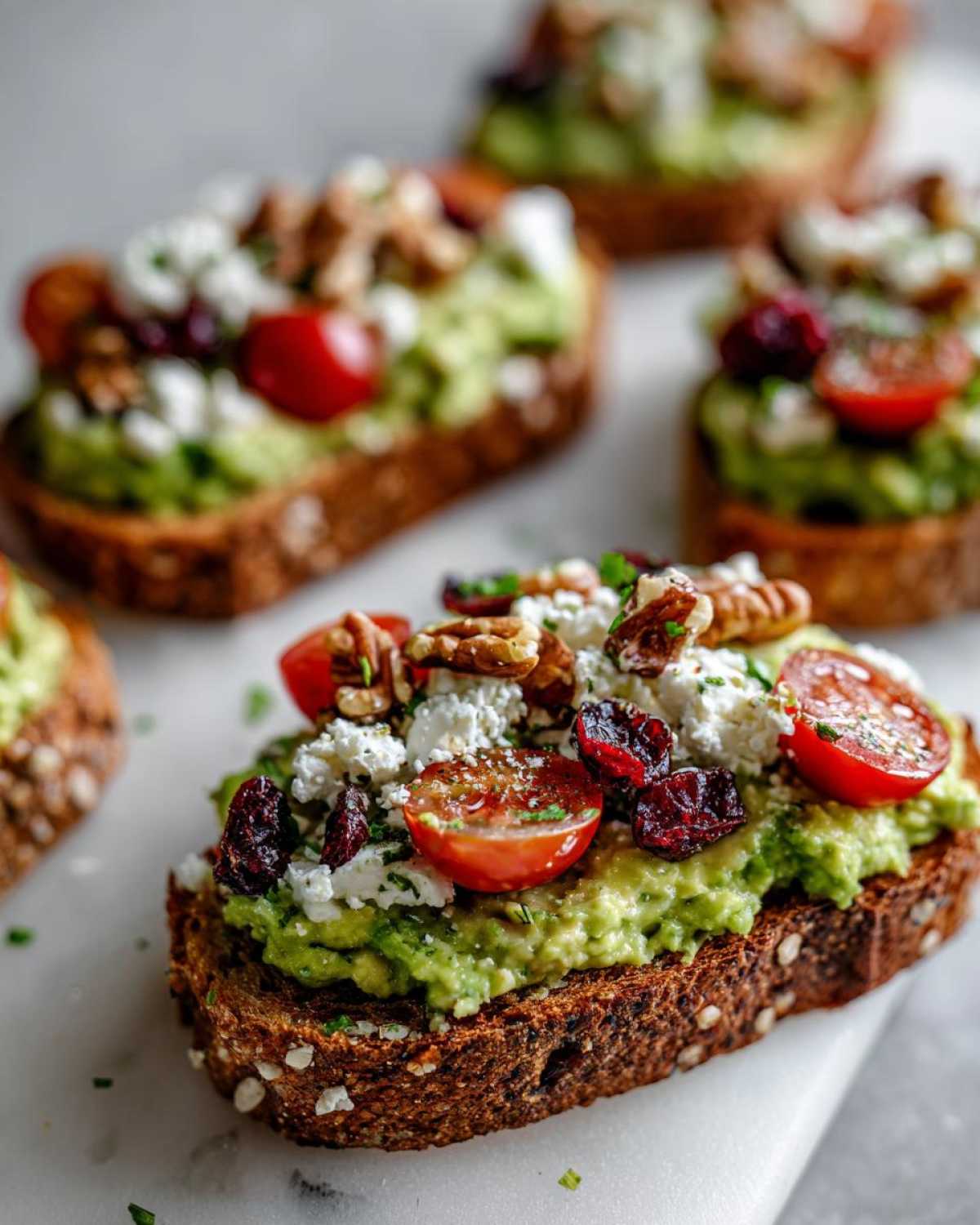 Close-up of avocado toast with feta cheese, cherry tomatoes, dried cranberries, and walnuts.