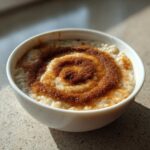 A white bowl filled with creamy banana oatmeal, topped with a distinct spiral pattern of brown sugar and cinnamon.