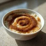 A white bowl filled with creamy banana oatmeal, topped with a distinct spiral pattern of brown sugar and cinnamon.
