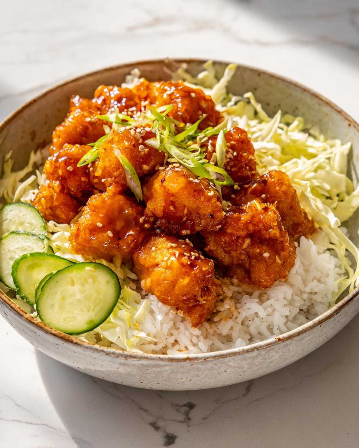 A close-up of delicious Bang Bang Salmon Bowls featuring crispy salmon bites over rice with shredded cabbage and cucumber slices.