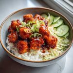 A close-up of Bang Bang Salmon Bowls featuring glazed salmon pieces over rice with shredded cabbage and cucumber slices.