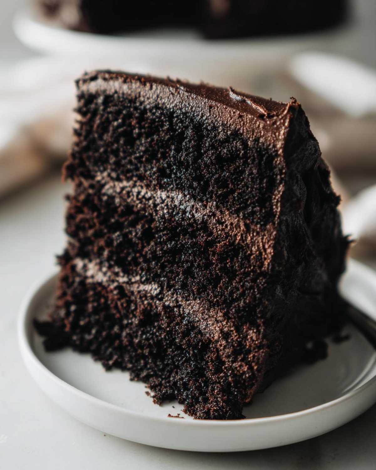A moist slice of black velvet halloween cake with rich chocolate frosting on a white plate.