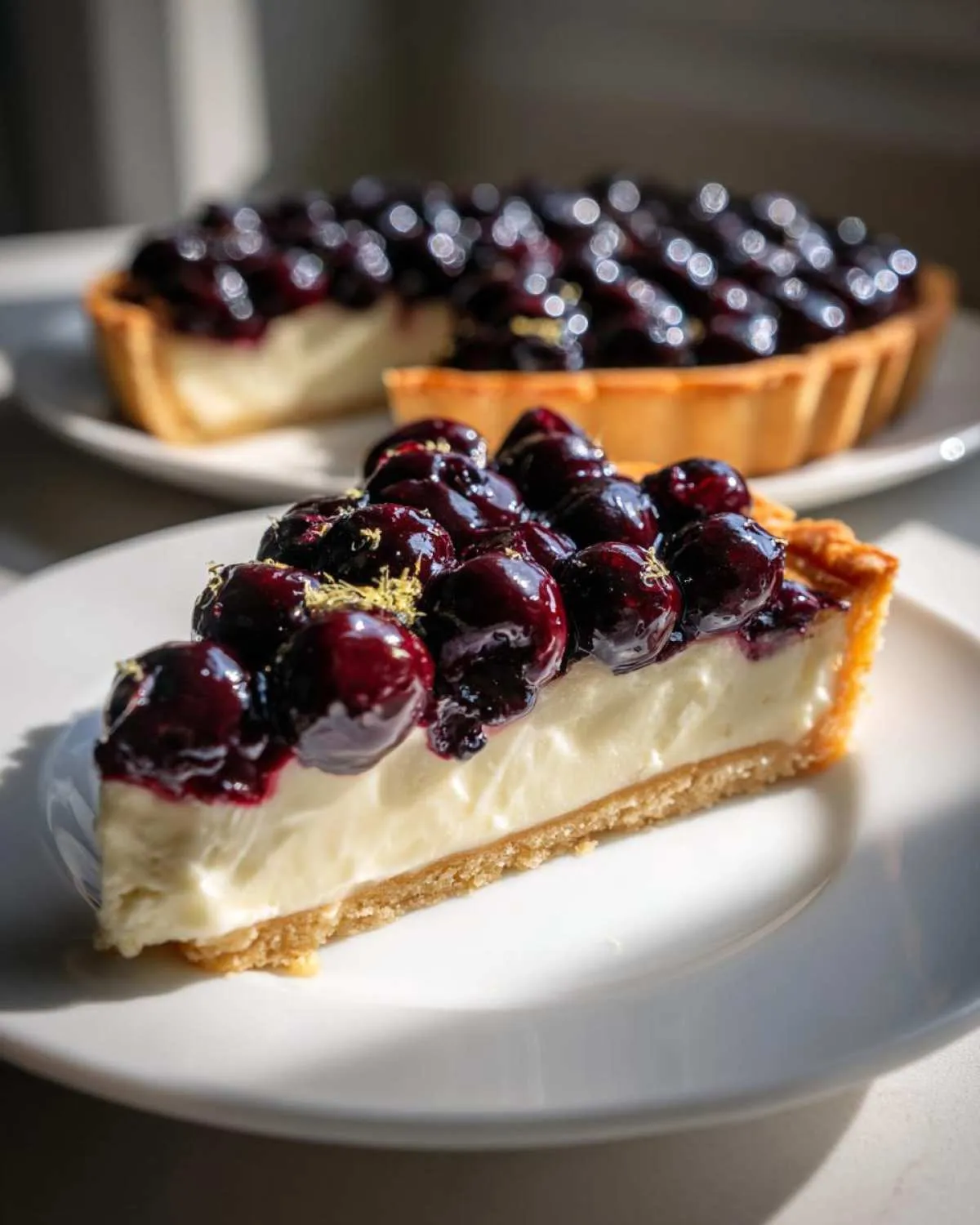 A slice of blueberry mascarpone tart on a white plate, topped with fresh blueberries and lemon zest.