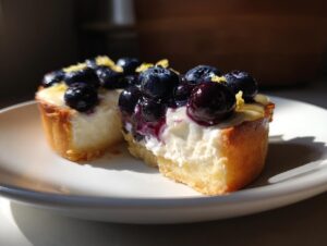 A close-up of a delicious blueberry mascarpone tart slice, topped with fresh blueberries and lemon zest.