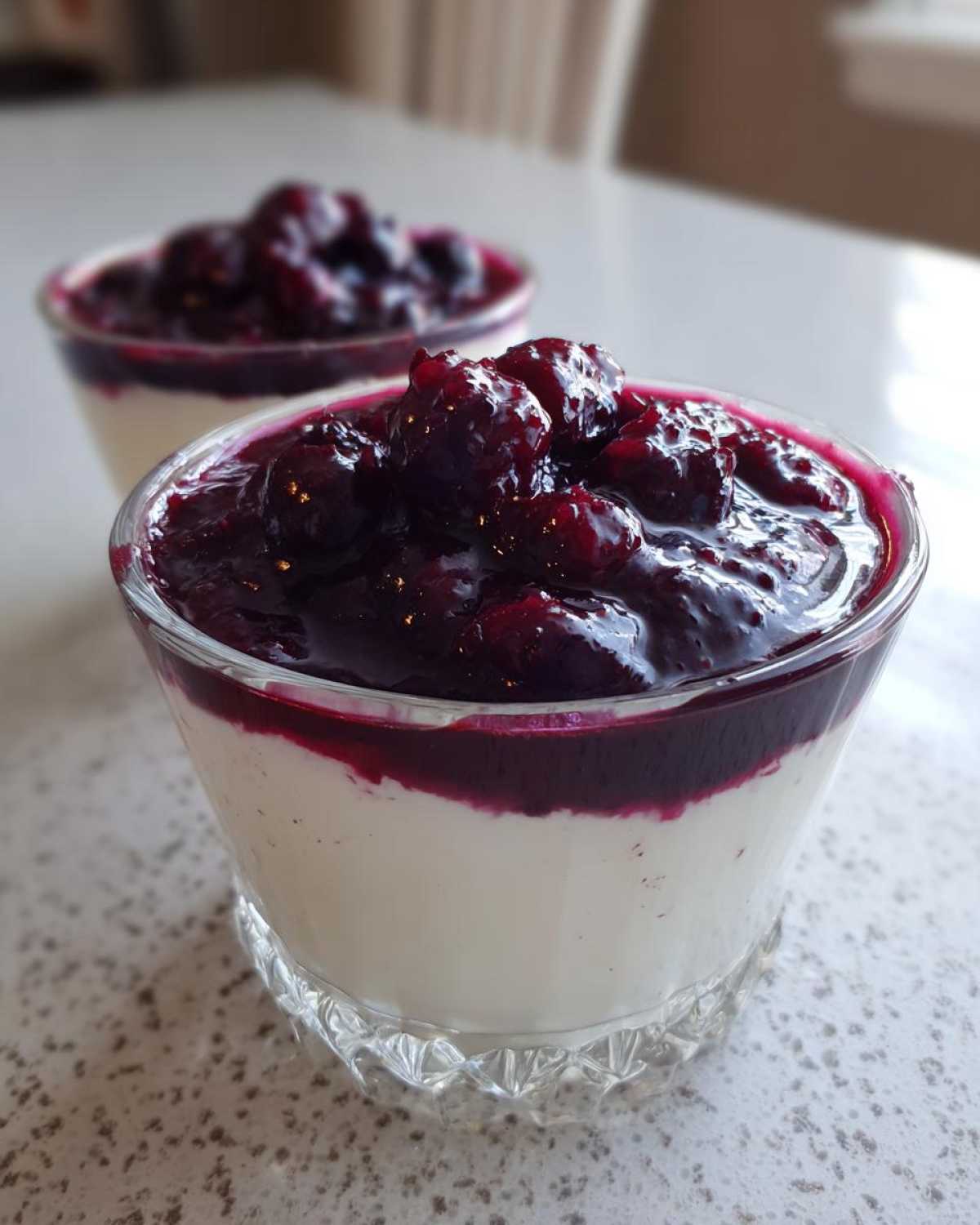 Close-up of a creamy Blueberry Vanilla Bean Panna Cotta topped with a rich blueberry compote in a glass dish.
