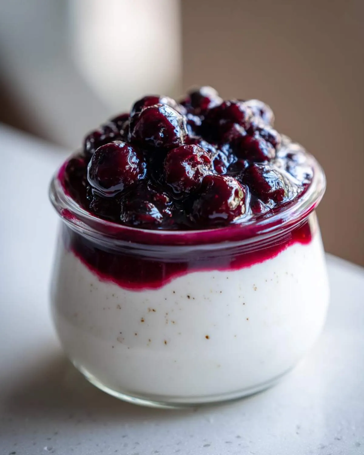 Close-up of a creamy Blueberry Vanilla Bean Panna Cotta in a glass jar, topped with fresh blueberries and sauce.