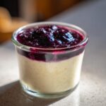 A close-up of a creamy Blueberry Vanilla Bean Panna Cotta in a glass jar, topped with a rich blueberry compote.