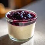 A close-up of a creamy Blueberry Vanilla Bean Panna Cotta in a glass jar, topped with a rich blueberry compote.