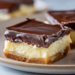 A close-up of a delicious Boston Cream Pie Fudge slice, showcasing its three distinct layers: a graham cracker crust, creamy vanilla filling, and rich chocolate ganache.