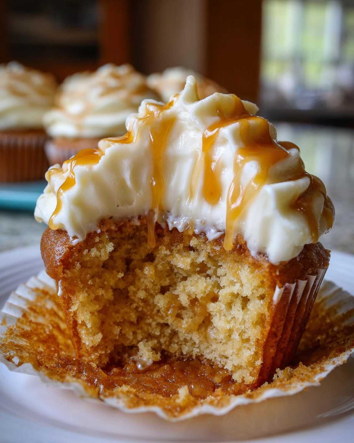 A close-up of a Butterbeer cupcake, cut in half, showing the moist crumb and topped with creamy frosting and caramel sauce.