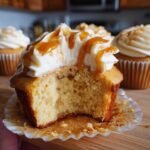 A close-up of a delicious Butterbeer cupcake with creamy frosting and caramel drizzle, with a bite taken out.