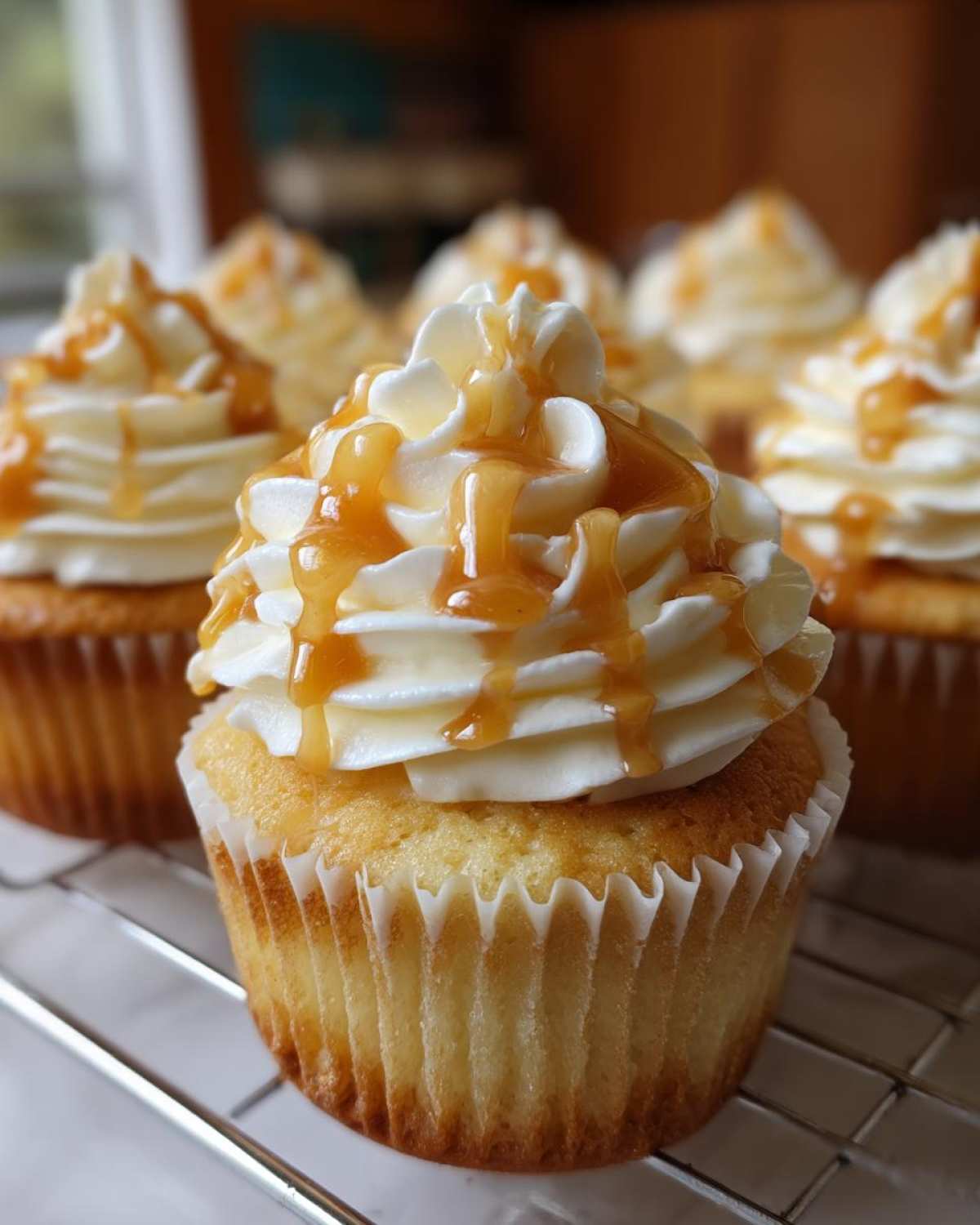 Close-up of a freshly baked Butterbeer cupcake topped with swirled white frosting and a rich caramel drizzle.