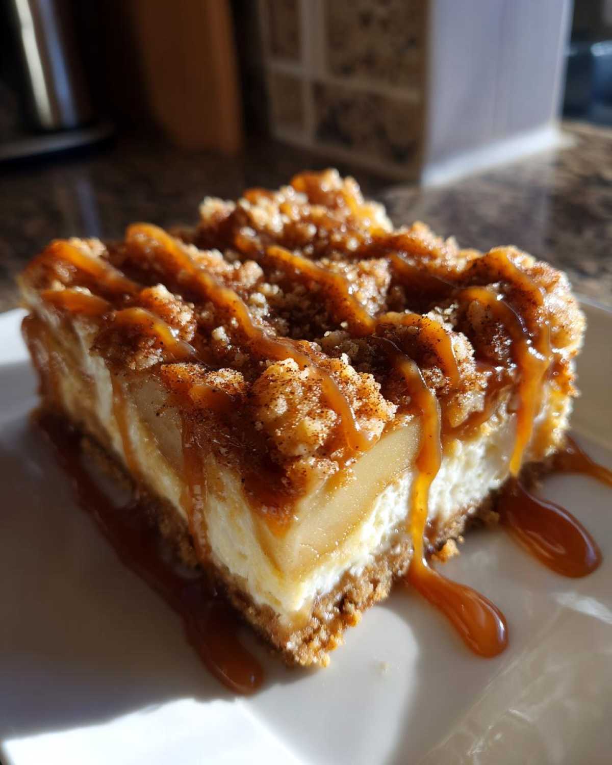 A delicious slice of caramel apple cheesecake bars, drizzled with caramel sauce and topped with crumble.