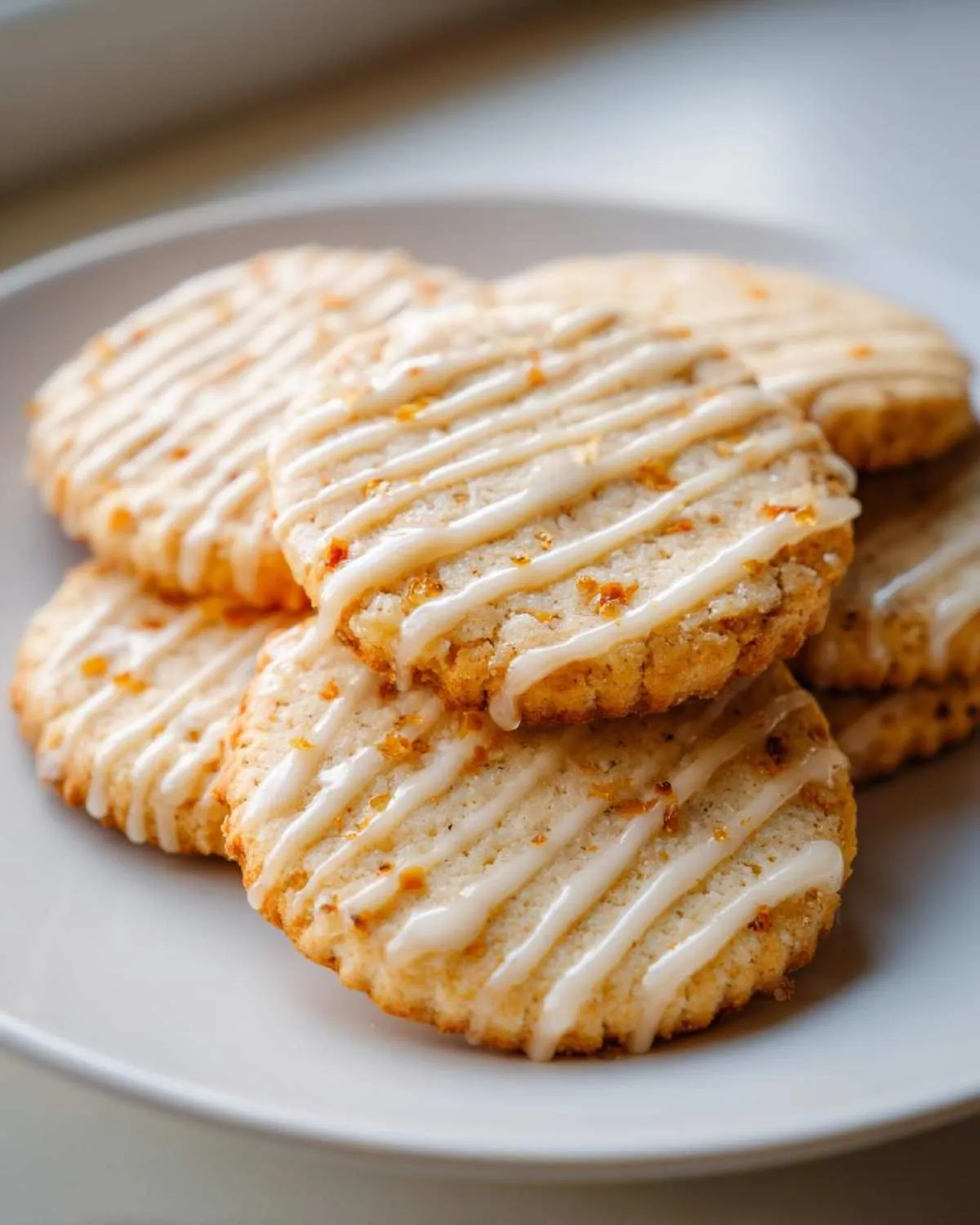 A stack of delicious cardamom shortbread cookies, drizzled with a white glaze and sprinkled with orange zest.
