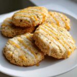 Close-up of cardamom shortbread cookies drizzled with white and golden glaze, sprinkled with green bits.