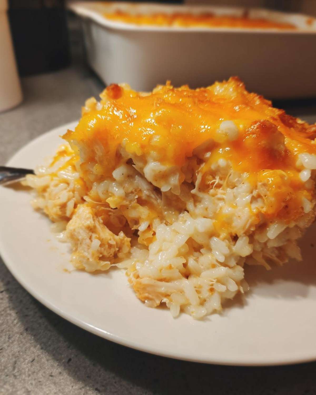 A close-up of a serving of creamy rice casserole topped with melted, golden cheddar cheese.