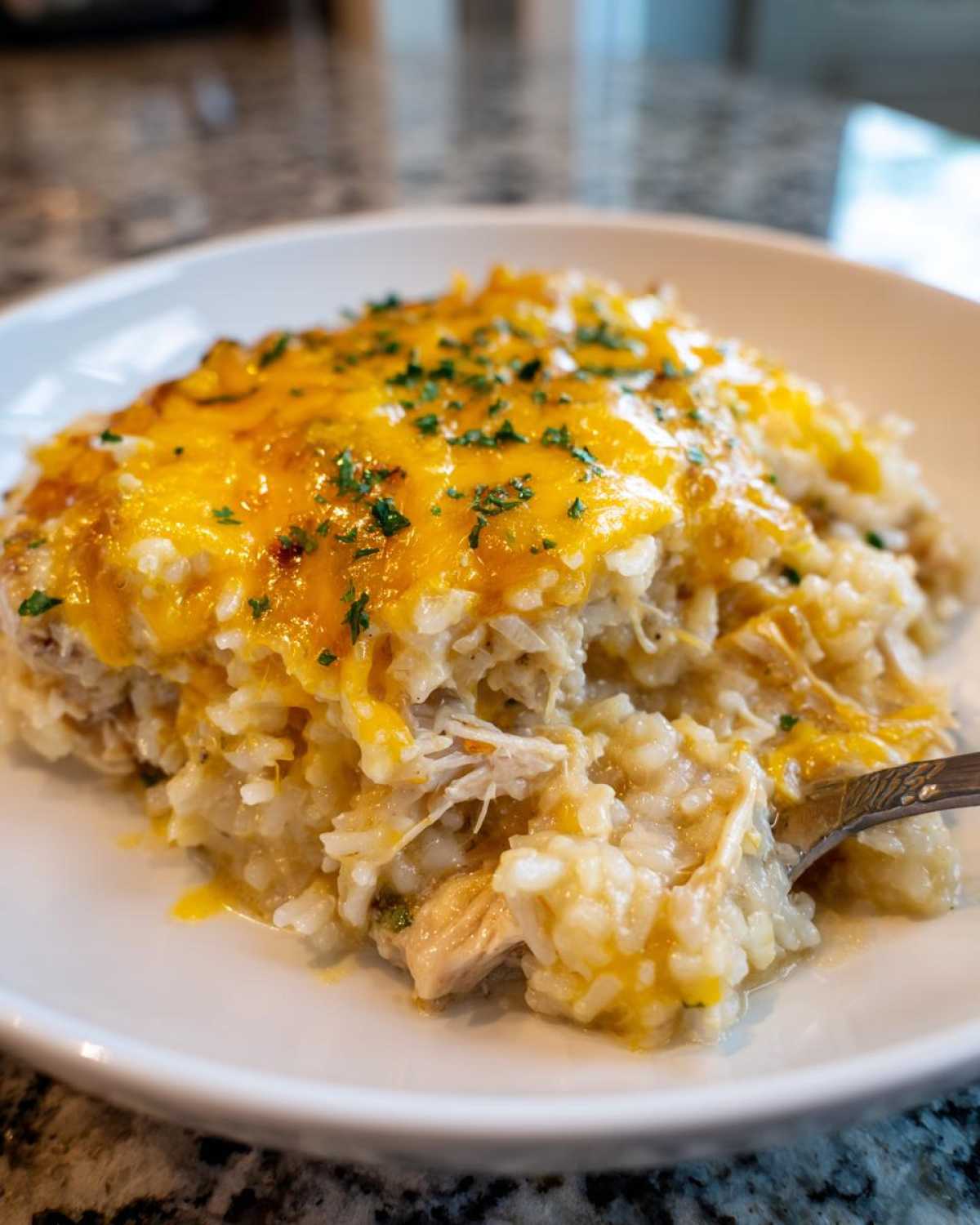 A close-up of a serving of creamy chicken rice casserole topped with melted cheddar cheese and fresh parsley.