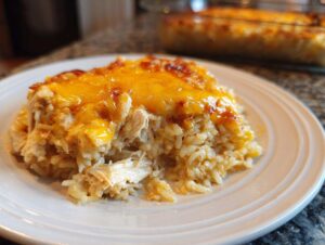 A close-up of a serving of creamy chicken rice casserole topped with melted, bubbly cheddar cheese.